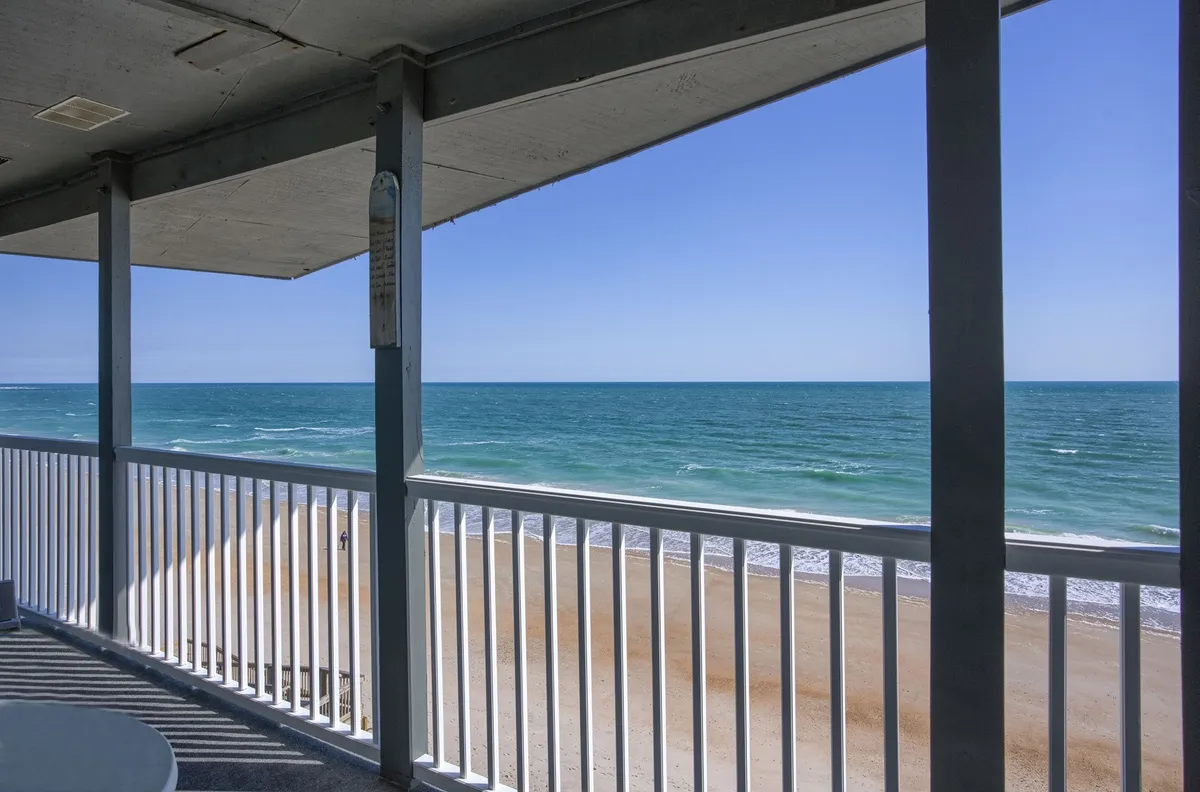 A peaceful view from the private balcony, showing the ocean, beach, and balcony railings. This inviting scene hints at Adirondack chairs and a pub table just out of frame, inviting guests to step outside and enjoy the breeze.