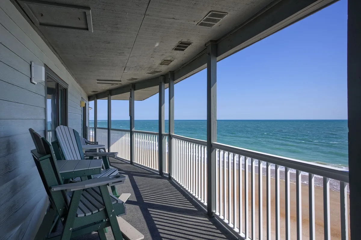 A pair of classic rocking chairs sit on a balcony or deck overlooking the ocean, framed by clean railings. The view sweeps out to the horizon, suggesting a peaceful place to relax after a day of activity.