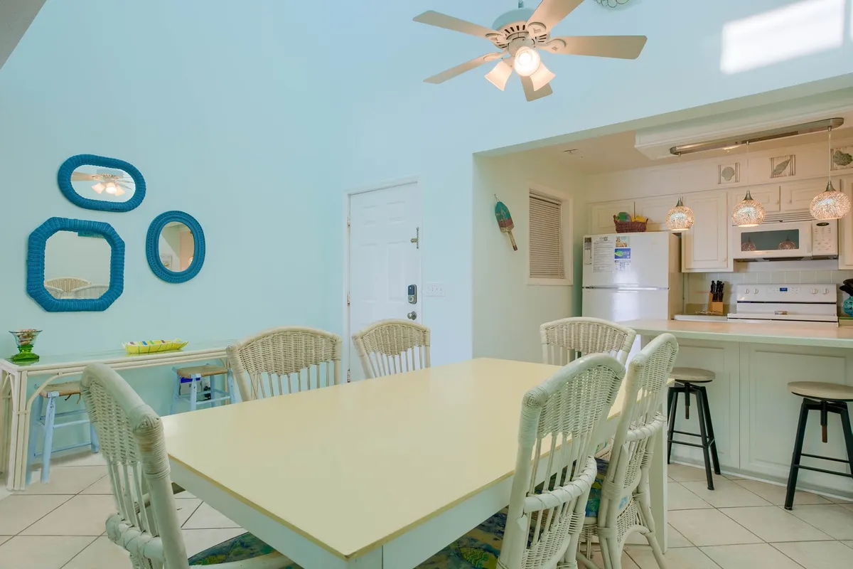 A spacious dining area with a large table set for family-style meals, highlighted by blue mirrors and stylish light fixtures. The kitchen entrance is visible, creating a sense of flow for entertaining and group dining.