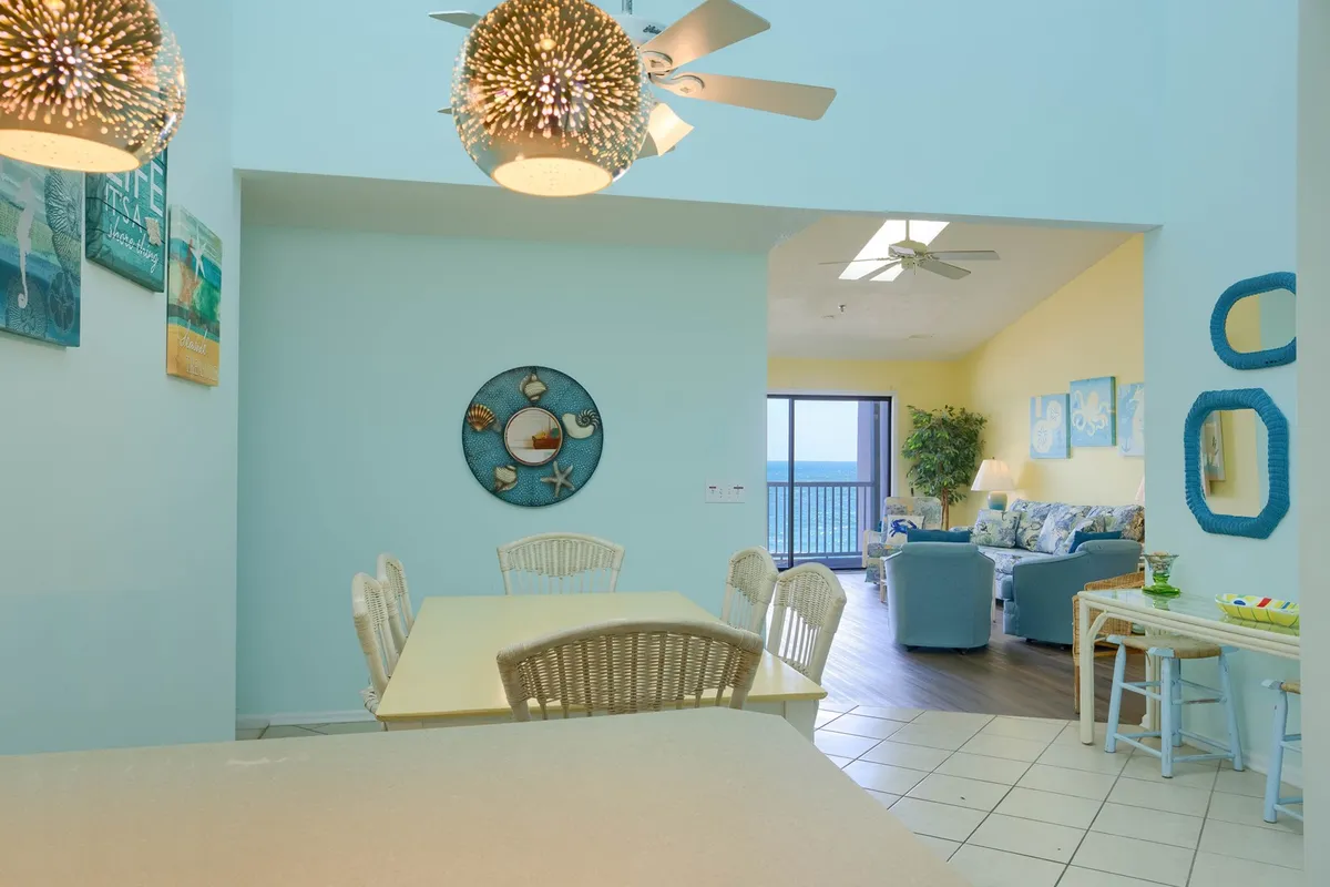 A dining area with a large table and decorative wall art, positioned to enjoy ocean views through wide windows. The space is inviting and full of natural light, making it perfect for family meals or casual gatherings after a day at the beach.